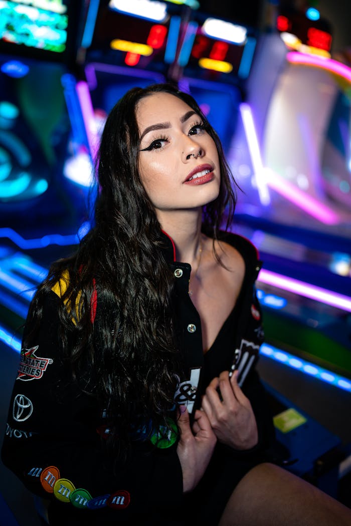 A fashionable woman poses confidently in a colorful arcade environment with neon lights.